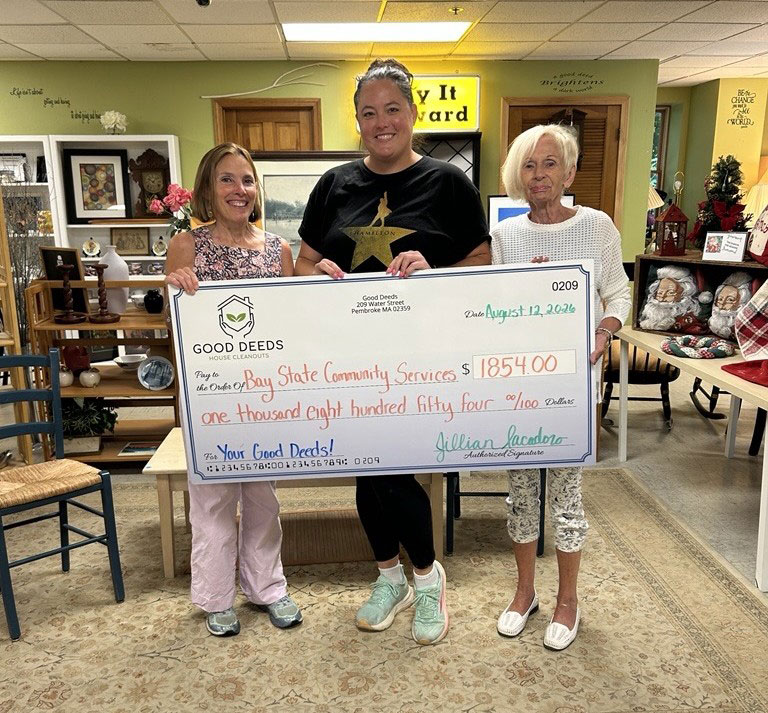 Three women holding a donation check for Bay State Community Services at Good Deeds Store.